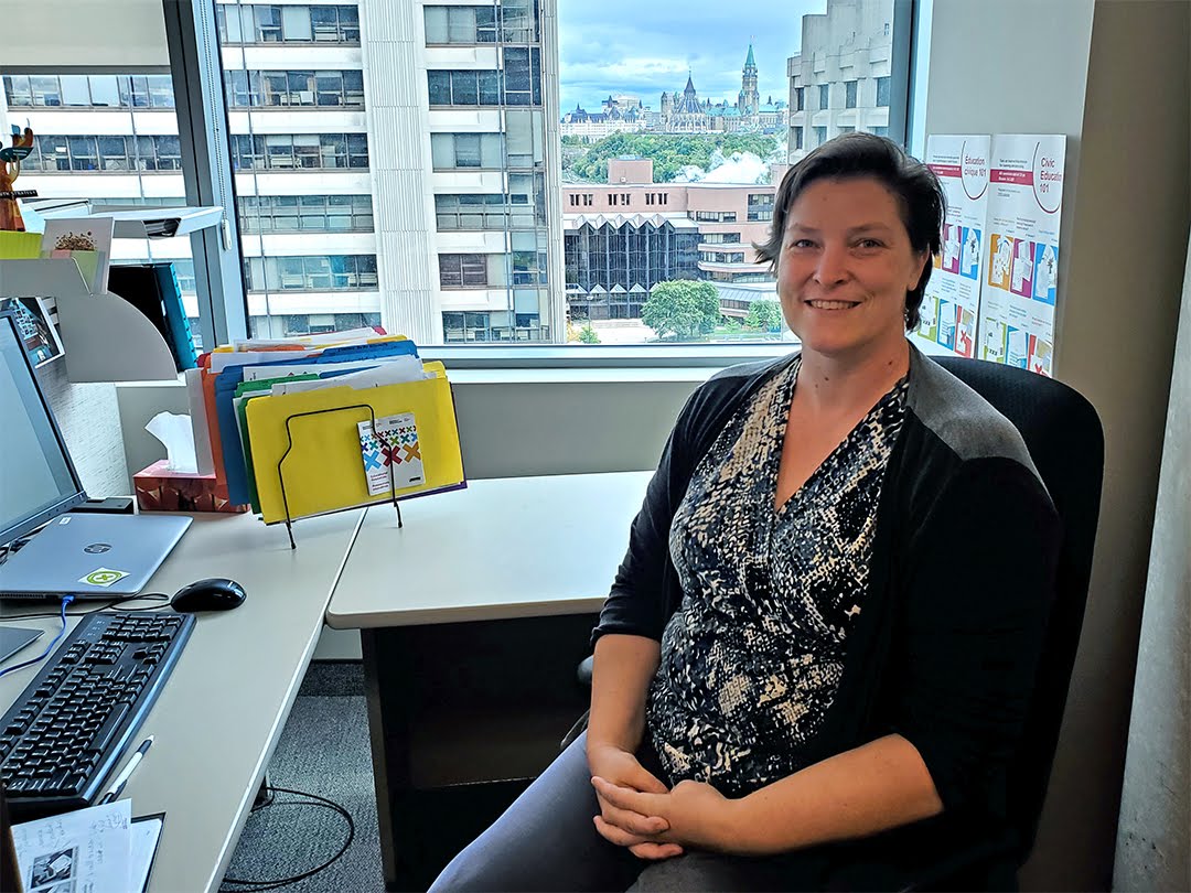 Rachel Collishaw at her desk at Elections Canada with Parliament in the background